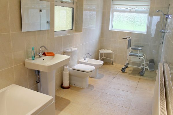 A spacious bathroom with a walk-in shower and a shower chair, wash basin and toilet with room to manoeuvre