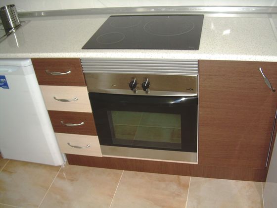 A close view of a built-in oven and ceramic hob set into a run of gloss units with a pale worktop