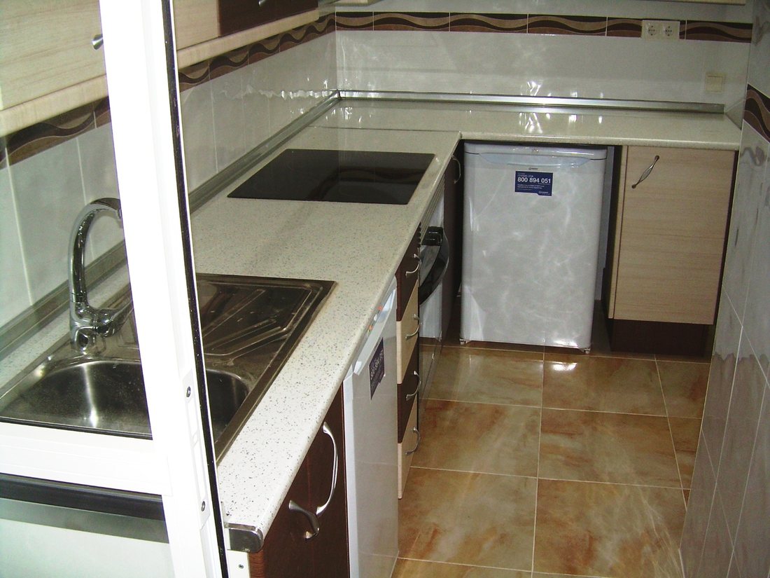 The corner of a fitted kitchen showing a stainless steel sink and mixer tap, a ceramic hob and cream gloss units