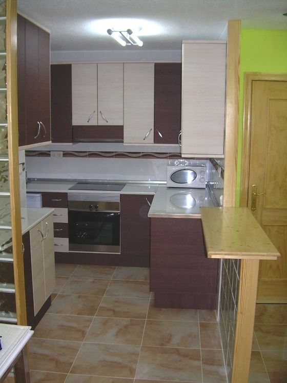 A kitchen in dark wood and cream with a built-in oven, a ceramic hob and a raised breakfast bar