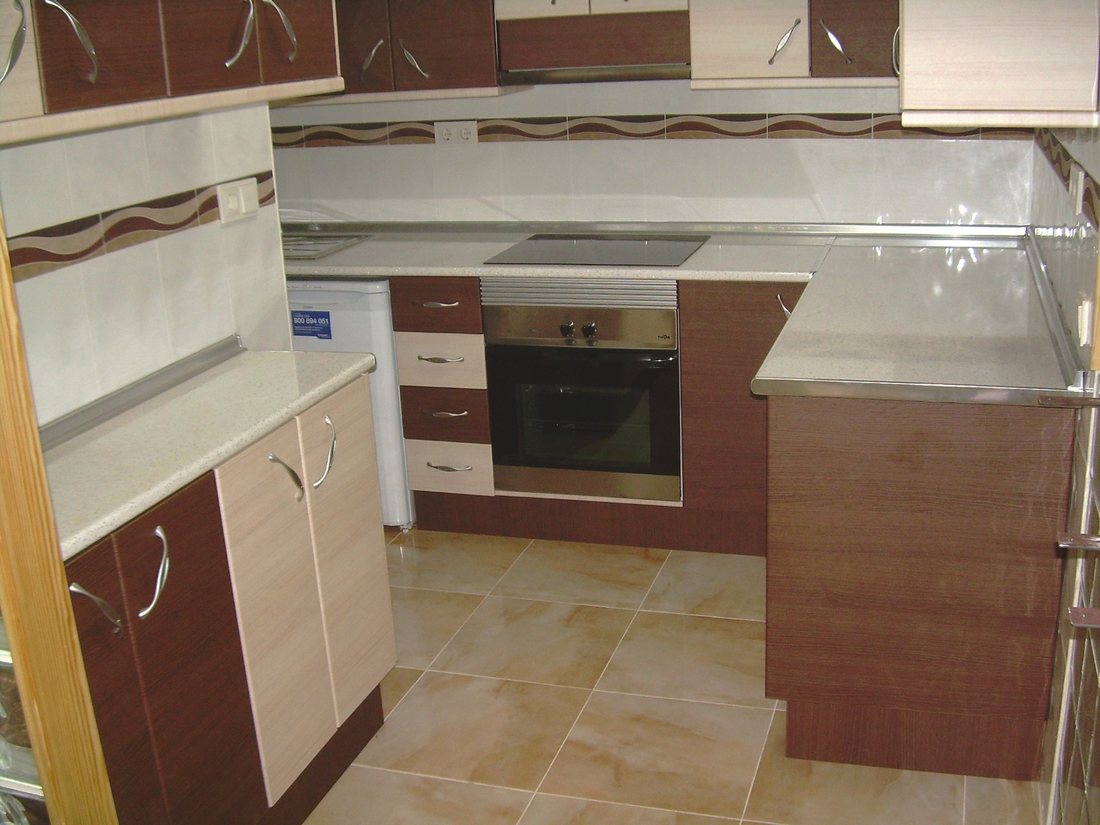 A fitted kitchen in cream and deep red gloss units with a pale worktop, a built-in oven and ceramic hob, and a decorative border tile above the counter