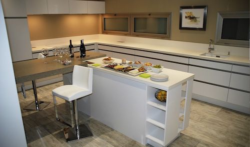 A handleless kitchen in grey and white with a peninsula breakfast bar, a bar stool and glass-fronted wall cabinets