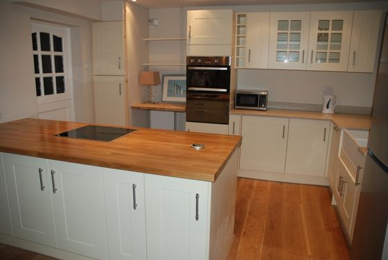 A cream shaker kitchen with a solid timber worktop on the island, a built-in double oven and microwave tower and glazed wall cabinets