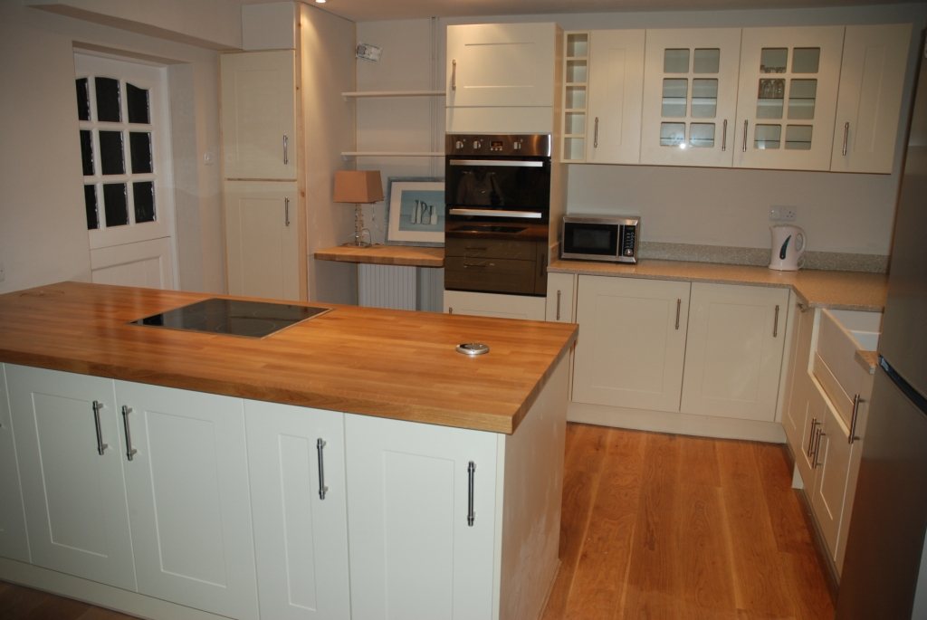 A cream shaker kitchen with a solid timber worktop on the island, a built-in double oven and microwave tower and glazed wall cabinets
