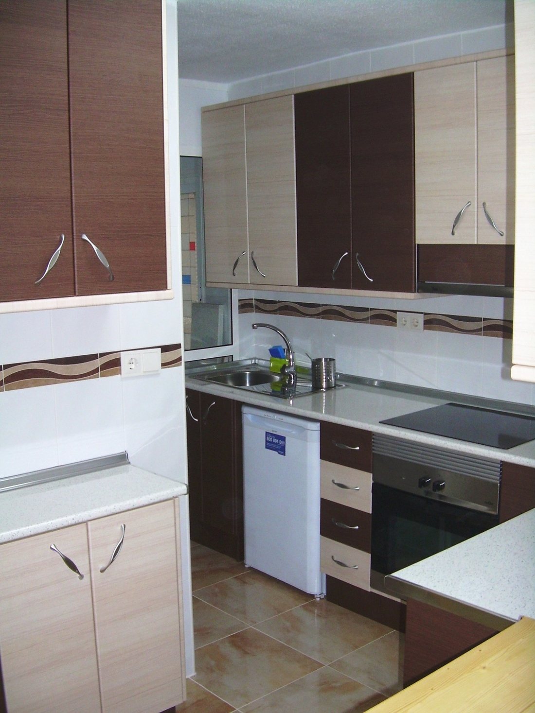 Dark wood wall units above cream base units, with the sink set under the window and an integrated hob