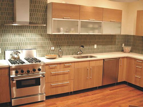 Timber-fronted kitchen units with a glass mosaic splashback, a range cooker beneath a stainless steel hood and an undermount sink