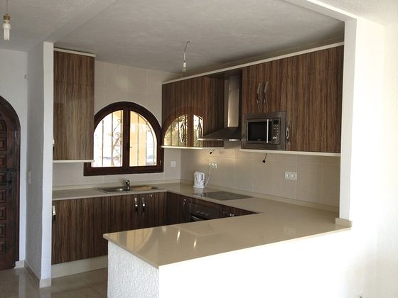 A U-shaped kitchen in dark walnut and cream with a pale quartz worktop, a peninsula breakfast bar and an arched window above the sink