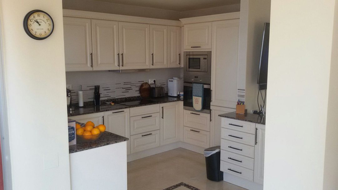 An L-shaped white shaker kitchen with a granite worktop and a built-in oven and microwave column