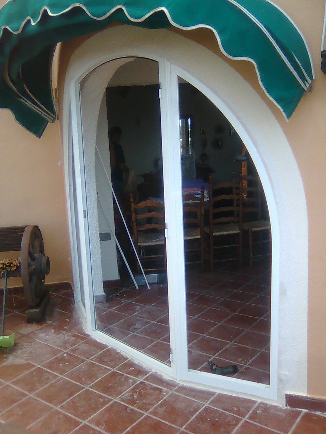 An arched white-framed glazed door opening onto a tiled terrace in a Spanish house, with a green awning above