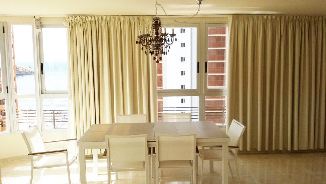 A dining room with tall white-framed windows, curtains and a chandelier